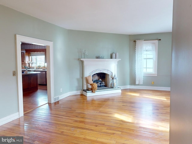 unfurnished living room featuring baseboards, a fireplace, light wood-style flooring, and a healthy amount of sunlight