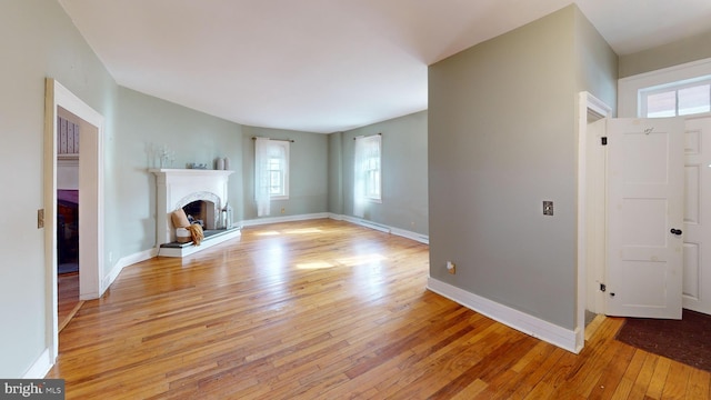 unfurnished living room featuring a fireplace with raised hearth, light wood-type flooring, and baseboards