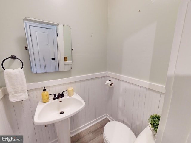 half bath with a wainscoted wall, wood finished floors, and toilet