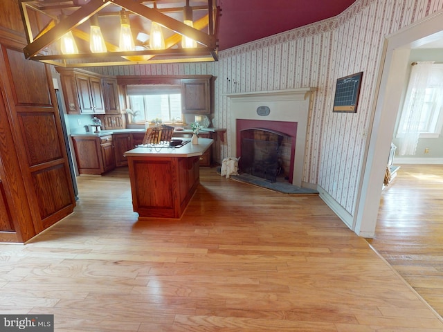 kitchen with a center island, brown cabinets, a fireplace with raised hearth, light wood-style floors, and wallpapered walls