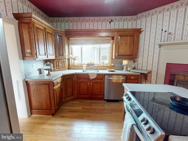 kitchen featuring stainless steel appliances, brown cabinetry, a sink, and wallpapered walls