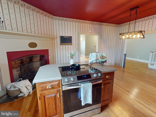 kitchen with wallpapered walls, brown cabinetry, stainless steel electric range oven, light wood-style flooring, and light countertops