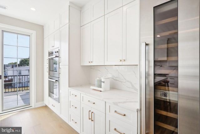 kitchen featuring light hardwood / wood-style flooring, double oven, white cabinets, light stone countertops, and backsplash