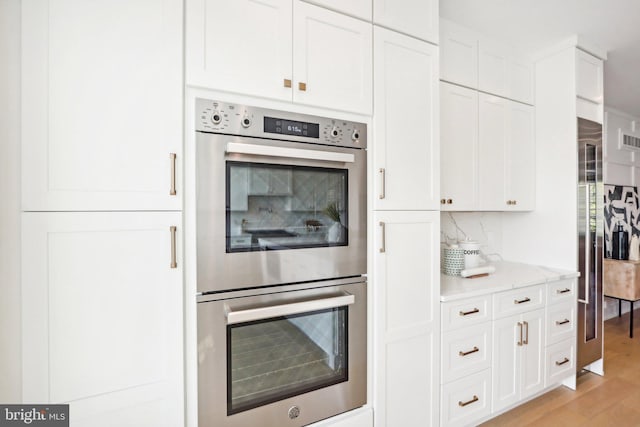 kitchen with white cabinetry, light hardwood / wood-style flooring, light stone countertops, and stainless steel double oven