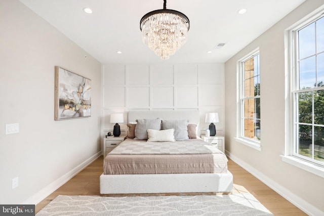 bedroom with multiple windows, light hardwood / wood-style flooring, and a chandelier