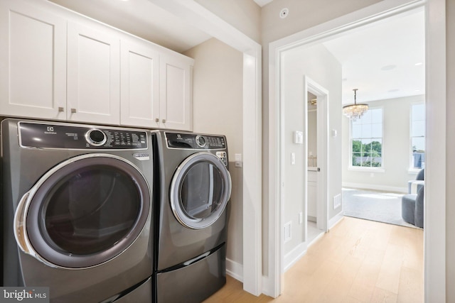 washroom featuring light hardwood / wood-style flooring, a notable chandelier, washer and clothes dryer, and cabinets