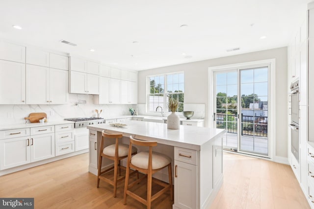 kitchen featuring a kitchen bar, a center island, light hardwood / wood-style flooring, decorative backsplash, and white cabinets