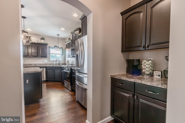 kitchen featuring sink, dark wood-type flooring, appliances with stainless steel finishes, hanging light fixtures, and dark brown cabinets