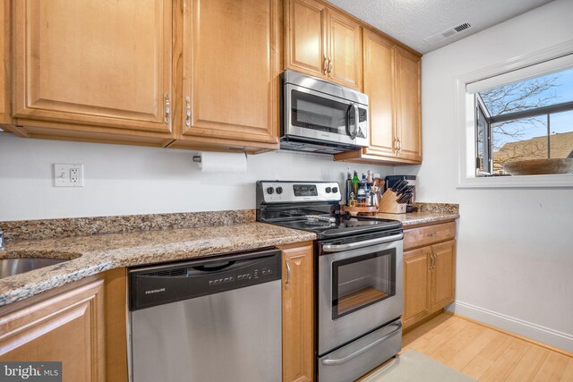 kitchen with sink, light hardwood / wood-style flooring, a textured ceiling, stainless steel appliances, and light stone countertops