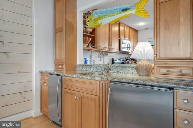 kitchen with light stone countertops, appliances with stainless steel finishes, sink, and light wood-type flooring