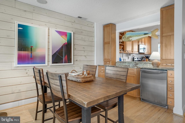 dining area featuring light hardwood / wood-style floors, a textured ceiling, and wood walls