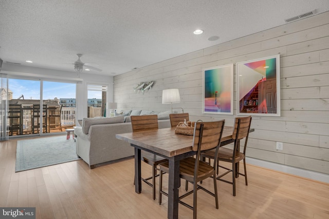 dining area featuring ceiling fan, wooden walls, a textured ceiling, and light wood-type flooring