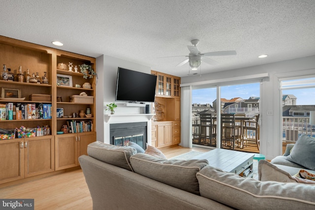 living room with ceiling fan, a wealth of natural light, a textured ceiling, and light hardwood / wood-style flooring