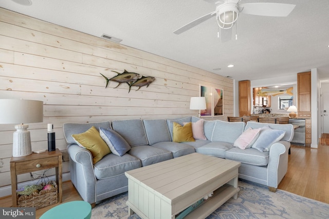 living room with ceiling fan, a textured ceiling, and light wood-type flooring