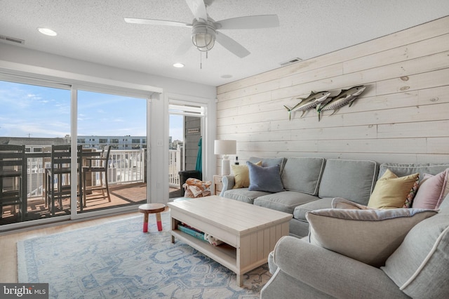 living room with hardwood / wood-style flooring, ceiling fan, wooden walls, and a textured ceiling