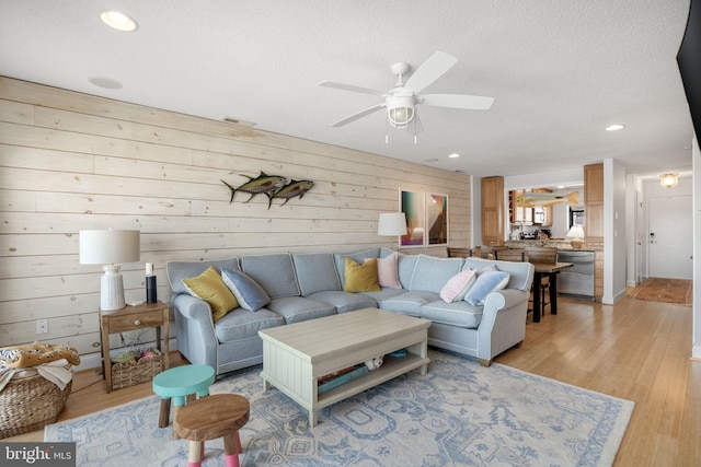 living room featuring ceiling fan, light hardwood / wood-style flooring, and a textured ceiling