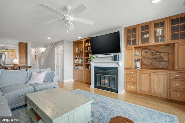 living room featuring ceiling fan, built in features, a textured ceiling, and light wood-type flooring