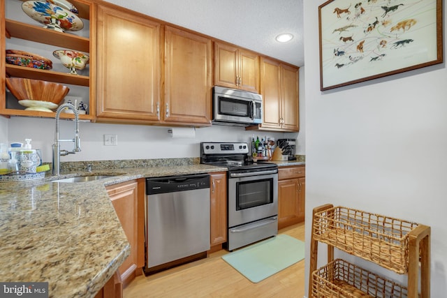 kitchen featuring sink, appliances with stainless steel finishes, light stone counters, a textured ceiling, and light wood-type flooring