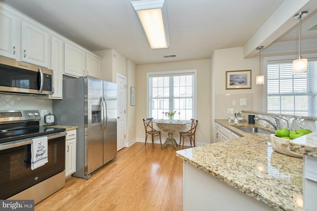 kitchen featuring visible vents, light wood finished floors, a sink, stainless steel appliances, and tasteful backsplash