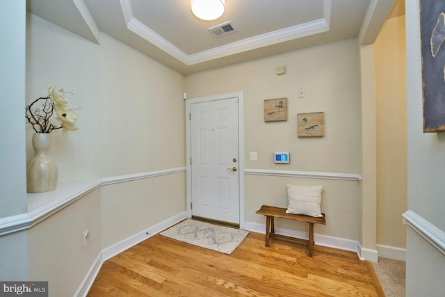 foyer featuring visible vents, wood finished floors, baseboards, crown molding, and a raised ceiling