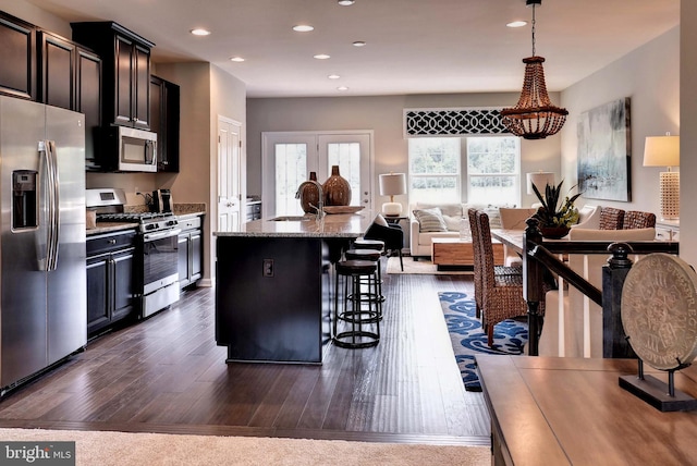 kitchen featuring sink, a breakfast bar, appliances with stainless steel finishes, light stone counters, and an island with sink