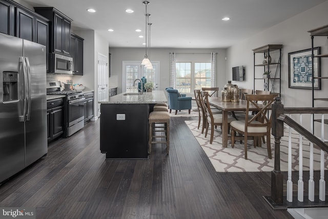 kitchen featuring light stone counters, hanging light fixtures, a kitchen breakfast bar, an island with sink, and stainless steel appliances