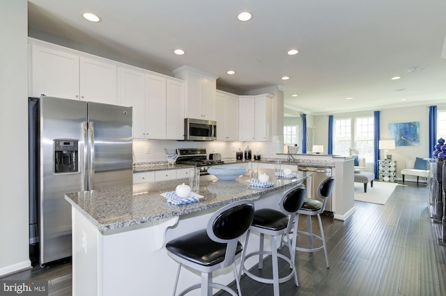 kitchen with a breakfast bar, white cabinetry, stainless steel appliances, light stone countertops, and a kitchen island