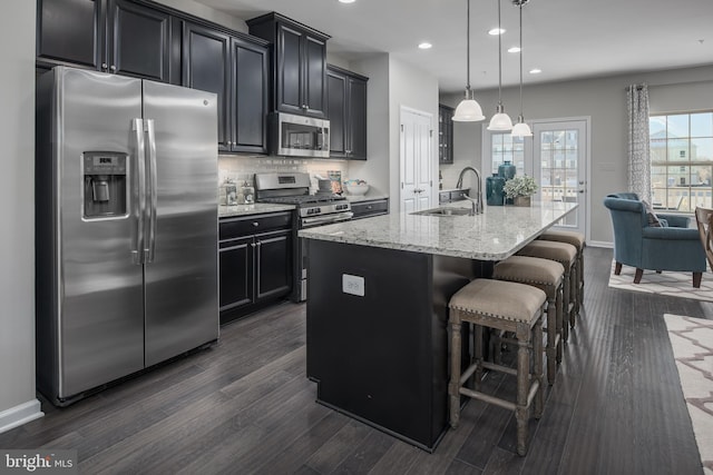 kitchen featuring sink, a breakfast bar area, appliances with stainless steel finishes, hanging light fixtures, and a center island with sink