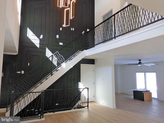 staircase featuring a high ceiling, hardwood / wood-style floors, and ceiling fan