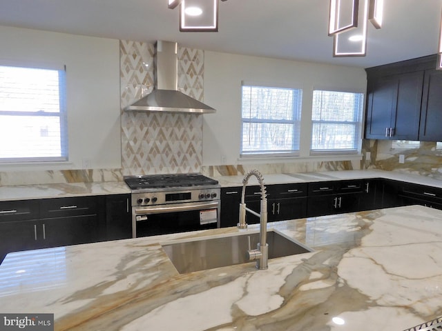 kitchen with tasteful backsplash, stainless steel gas range oven, light stone counters, and wall chimney exhaust hood