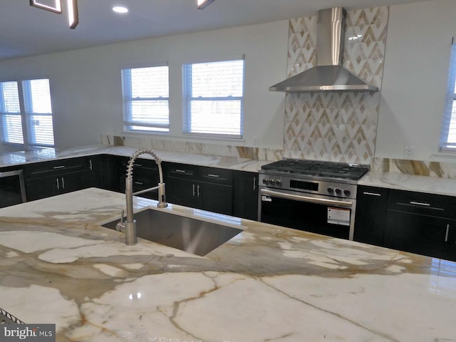 kitchen with wall chimney range hood, sink, stainless steel gas range, light stone countertops, and a healthy amount of sunlight