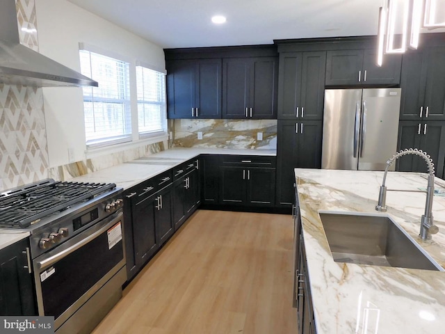 kitchen featuring appliances with stainless steel finishes, range hood, sink, decorative backsplash, and light stone countertops