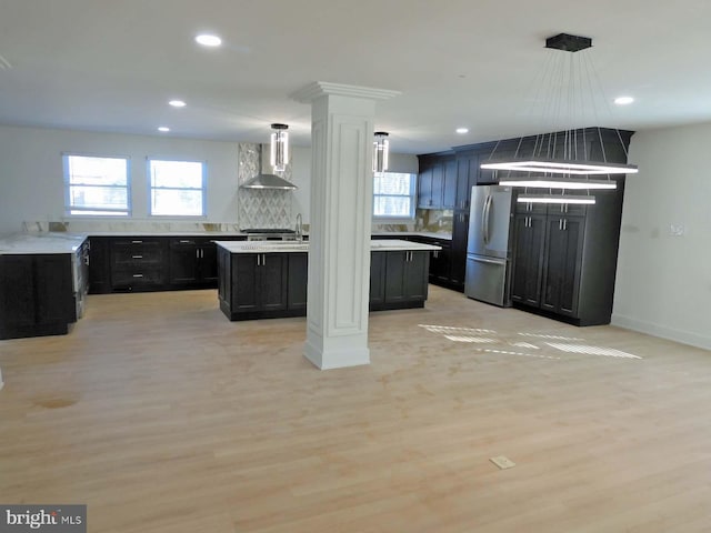 kitchen featuring wall chimney exhaust hood, decorative columns, a center island, stainless steel refrigerator, and light hardwood / wood-style floors