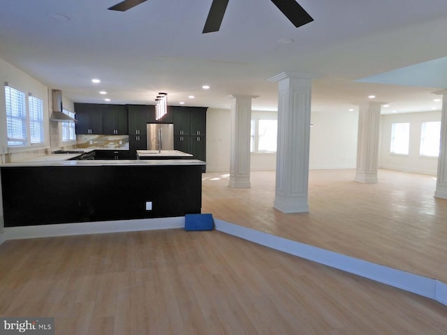 kitchen featuring stainless steel fridge, kitchen peninsula, wall chimney exhaust hood, and ornate columns