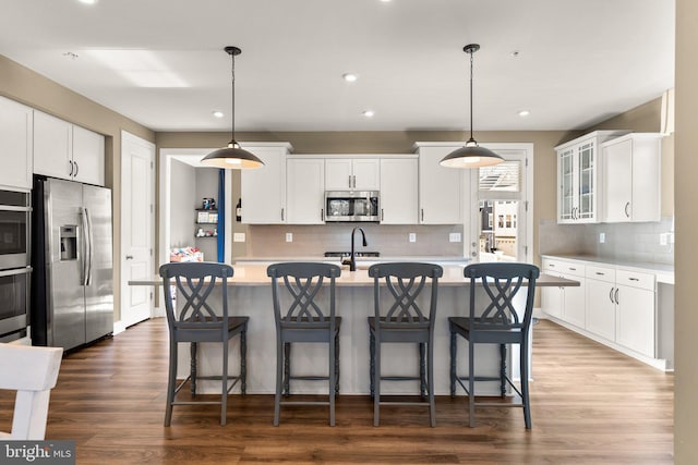 kitchen featuring stainless steel appliances, hanging light fixtures, a center island with sink, and white cabinets