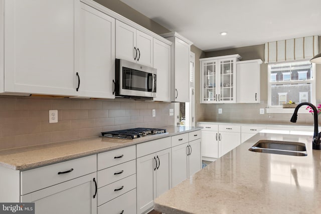 kitchen with appliances with stainless steel finishes, sink, white cabinets, backsplash, and light stone counters