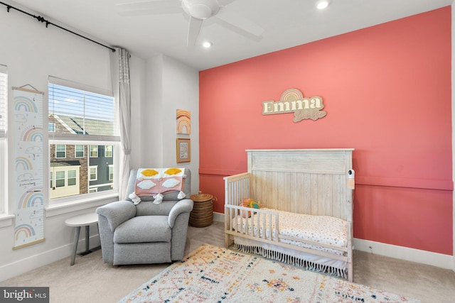 bedroom featuring a nursery area, ceiling fan, and light colored carpet