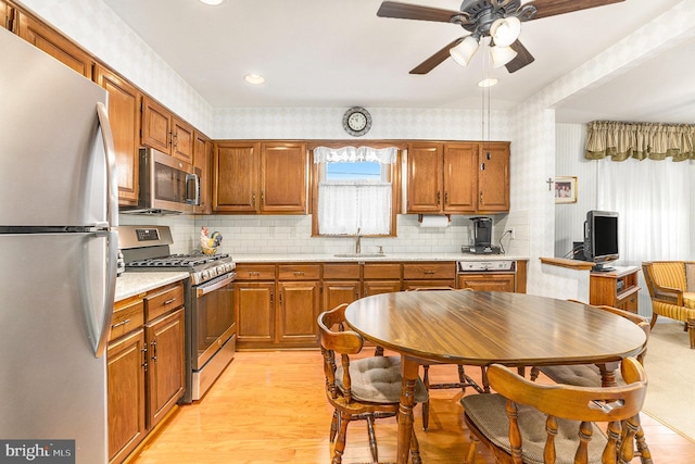 kitchen with appliances with stainless steel finishes, sink, backsplash, ceiling fan, and light hardwood / wood-style flooring