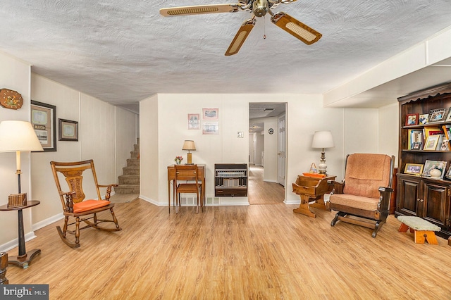 sitting room with ceiling fan, heating unit, a textured ceiling, and light wood-type flooring