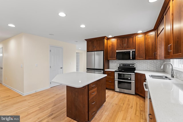 kitchen featuring appliances with stainless steel finishes, sink, backsplash, a center island, and light wood-type flooring