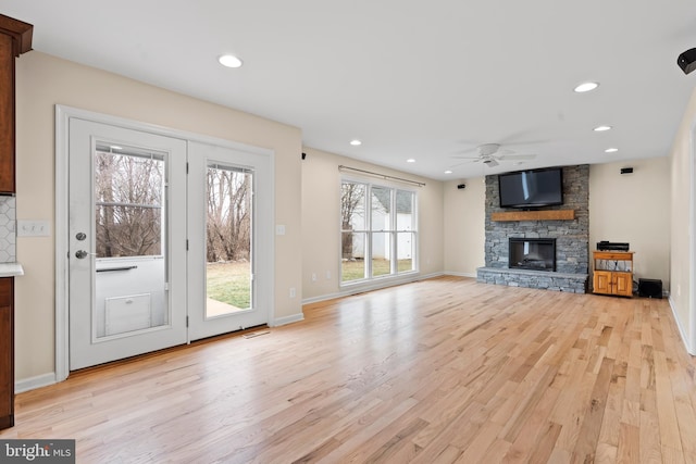 unfurnished living room featuring a stone fireplace, ceiling fan, and light wood-type flooring