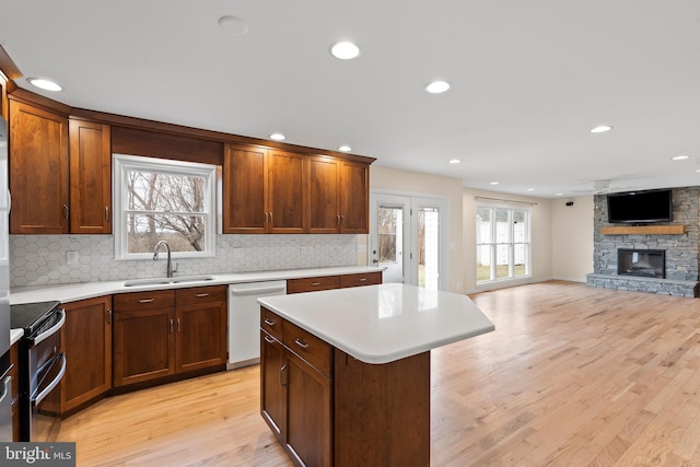 kitchen featuring a stone fireplace, dishwasher, sink, double oven range, and a center island