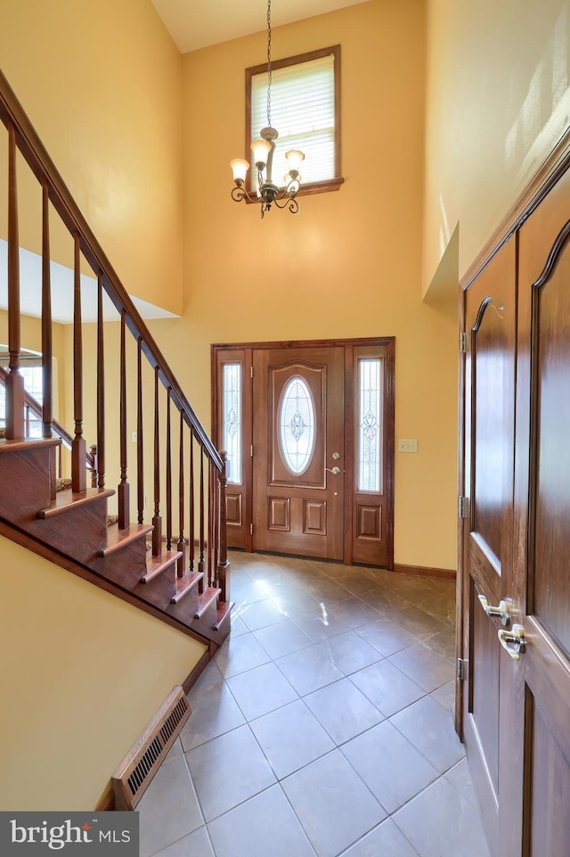 foyer with stairs, a towering ceiling, visible vents, a chandelier, and tile patterned flooring