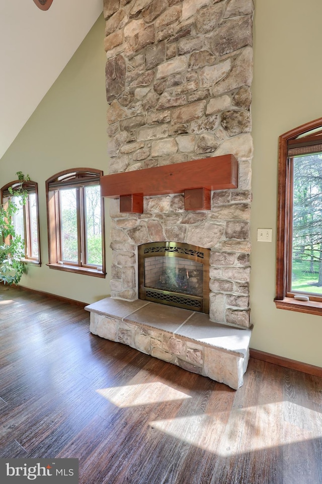 living room with baseboards, a stone fireplace, high vaulted ceiling, and wood finished floors