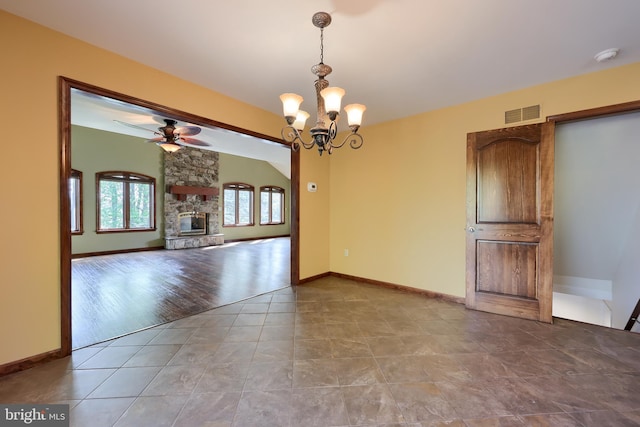 unfurnished dining area with ceiling fan with notable chandelier, visible vents, tile patterned flooring, baseboards, and a stone fireplace