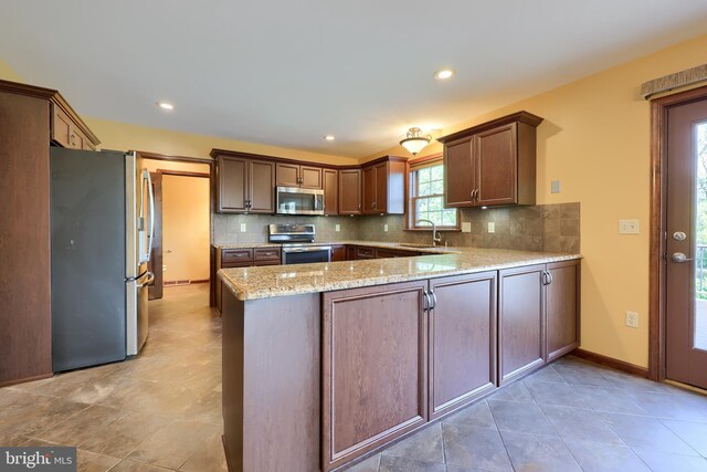kitchen with a sink, a peninsula, backsplash, and appliances with stainless steel finishes