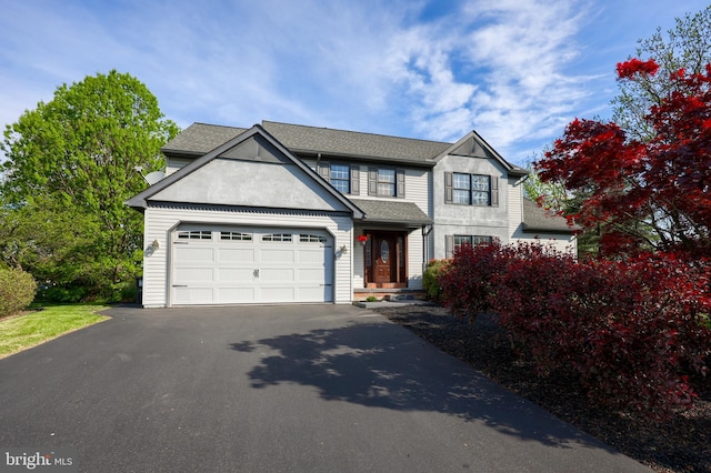 traditional-style home featuring an attached garage, a shingled roof, and driveway