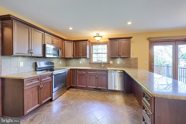 kitchen with a sink, a peninsula, light stone counters, backsplash, and appliances with stainless steel finishes