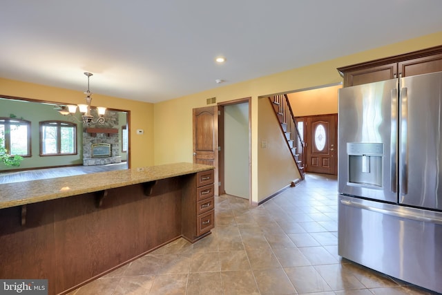 kitchen featuring stainless steel refrigerator with ice dispenser, an inviting chandelier, light tile patterned floors, light stone countertops, and hanging light fixtures