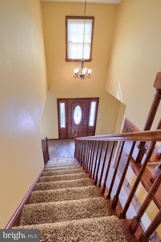 stairs with a towering ceiling, a wealth of natural light, and a notable chandelier